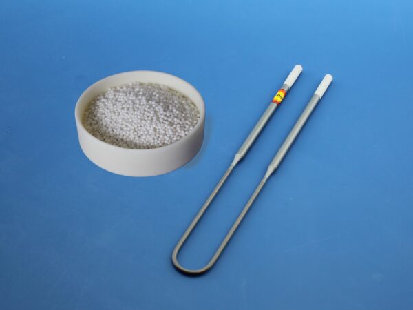 White spherical pellets in a dish beside two metallic stirring rods against a blue background, suggesting a laboratory or chemical context.